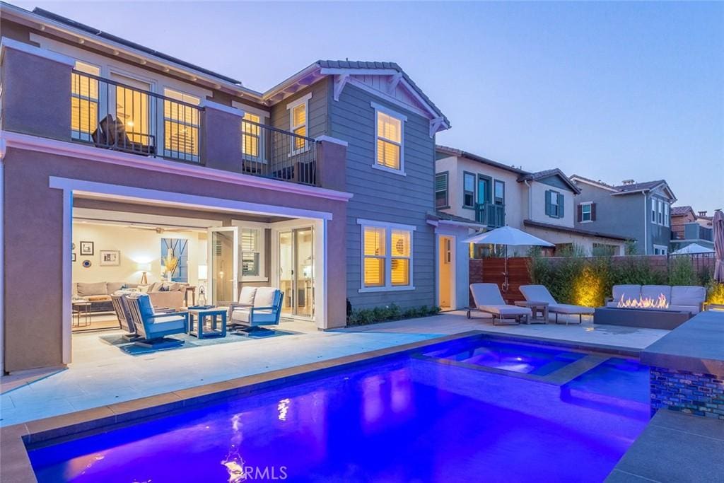 pool at dusk with an in ground hot tub, an outdoor living space with a fire pit, and a patio