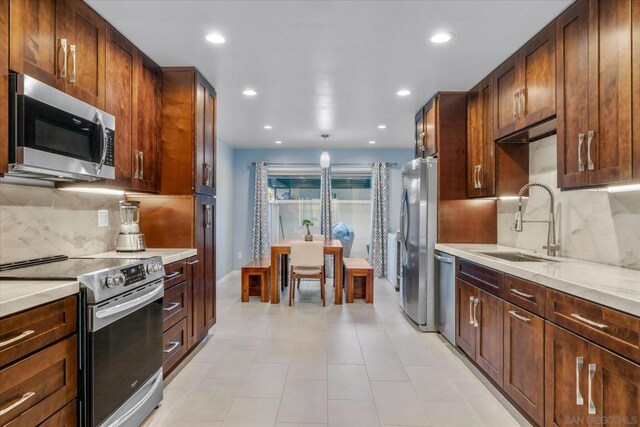 kitchen with tasteful backsplash, light stone countertops, appliances with stainless steel finishes, and sink