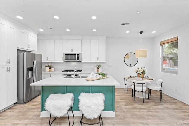 kitchen featuring white cabinets, appliances with stainless steel finishes, tasteful backsplash, an island with sink, and hanging light fixtures