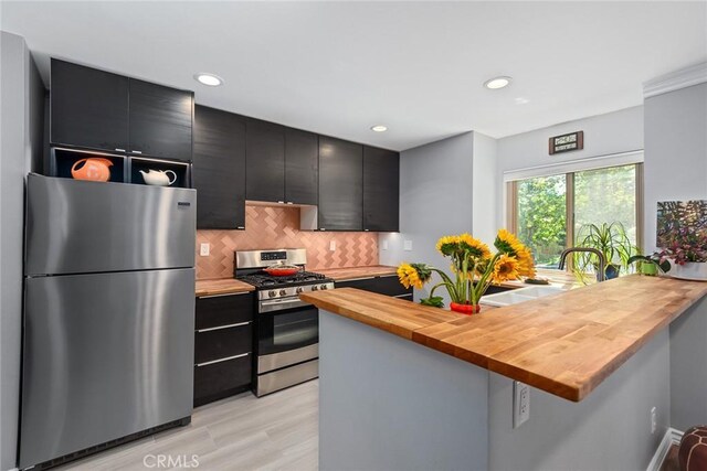 kitchen featuring kitchen peninsula, sink, light wood-type flooring, appliances with stainless steel finishes, and butcher block counters