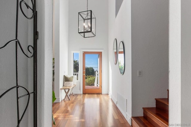 foyer entrance featuring light wood-type flooring, a towering ceiling, and a chandelier