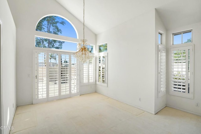 spare room with high vaulted ceiling, a wealth of natural light, and a chandelier