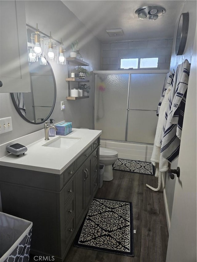 full bathroom with hardwood / wood-style flooring, bath / shower combo with glass door, toilet, and vanity
