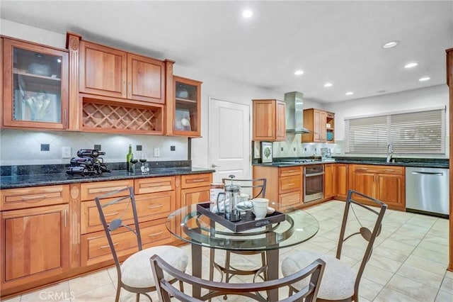 kitchen with decorative backsplash, wall chimney range hood, appliances with stainless steel finishes, and dark stone countertops