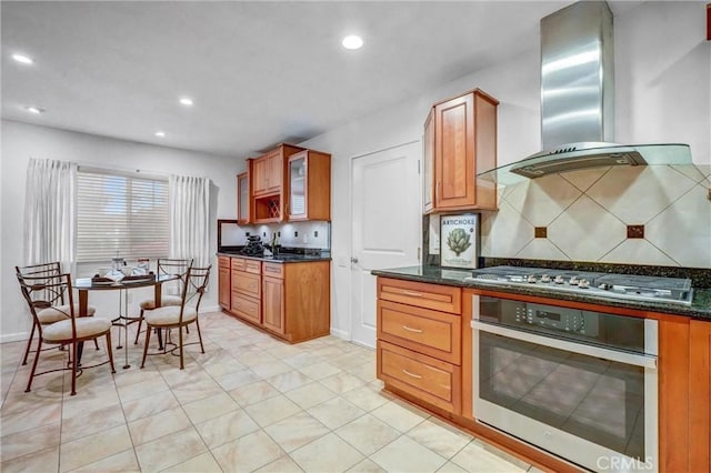 kitchen featuring decorative backsplash, appliances with stainless steel finishes, wall chimney range hood, and dark stone counters