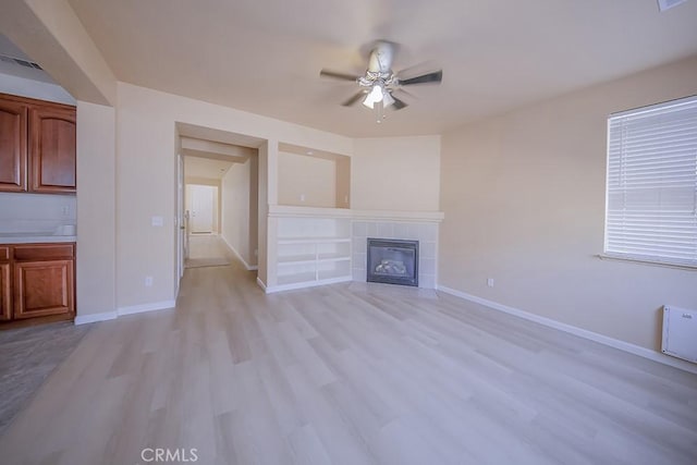 unfurnished living room featuring ceiling fan, a tile fireplace, and light hardwood / wood-style flooring