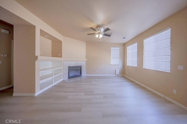 unfurnished living room with ceiling fan, a tiled fireplace, and light wood-type flooring