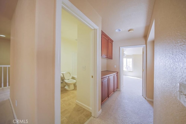 hallway featuring light colored carpet and a textured ceiling