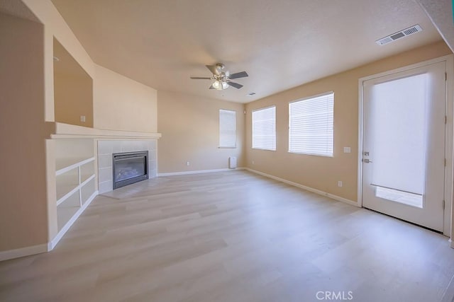 unfurnished living room featuring ceiling fan, a tiled fireplace, and light wood-type flooring