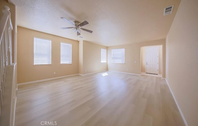 empty room with ceiling fan, a wealth of natural light, light hardwood / wood-style flooring, and a textured ceiling