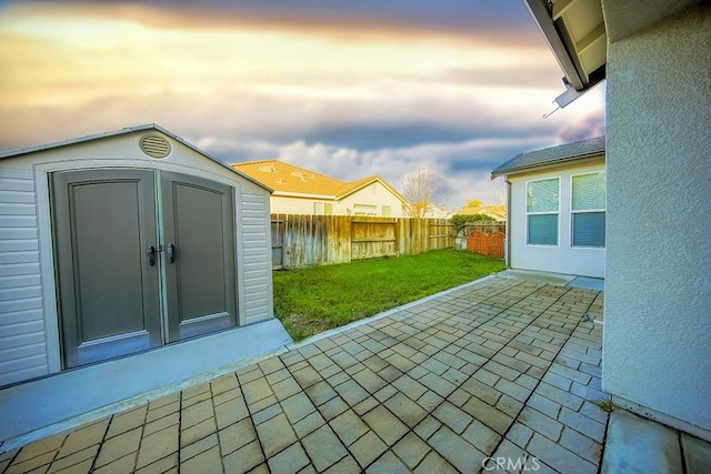 patio terrace at dusk featuring a storage unit and a yard