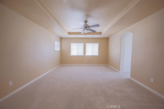 empty room featuring ceiling fan, light colored carpet, a textured ceiling, and a tray ceiling