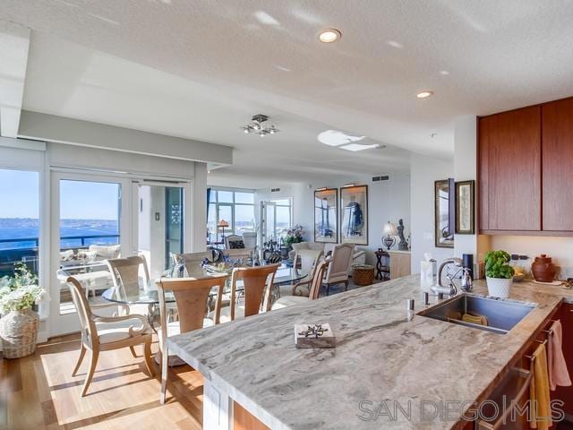 kitchen with kitchen peninsula, light wood-type flooring, a textured ceiling, a water view, and sink