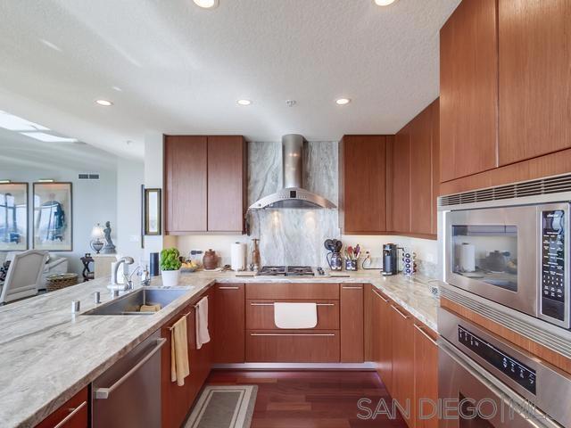 kitchen featuring stainless steel appliances, dark hardwood / wood-style floors, light stone countertops, wall chimney exhaust hood, and sink