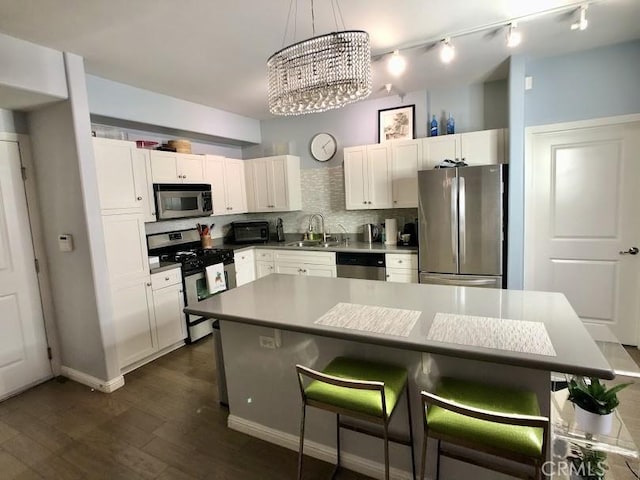 kitchen with appliances with stainless steel finishes, a kitchen island, white cabinetry, sink, and a chandelier