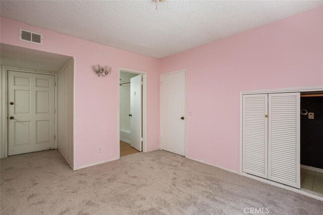 unfurnished bedroom featuring ensuite bathroom, a closet, light carpet, and a textured ceiling