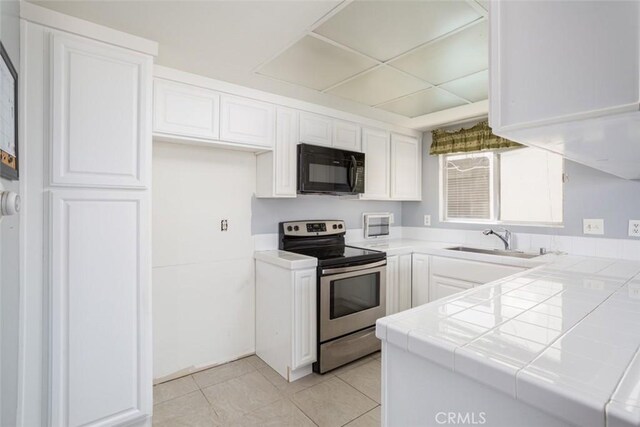 kitchen featuring stainless steel electric range, sink, light tile patterned flooring, white cabinetry, and tile counters