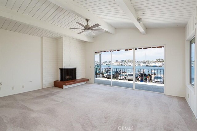 unfurnished living room with a brick fireplace, ceiling fan, light colored carpet, vaulted ceiling with beams, and a water view