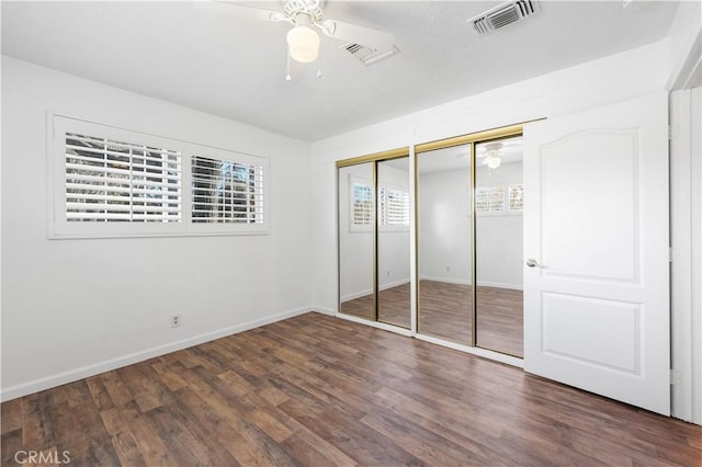 unfurnished bedroom with dark wood-type flooring, ceiling fan, and two closets