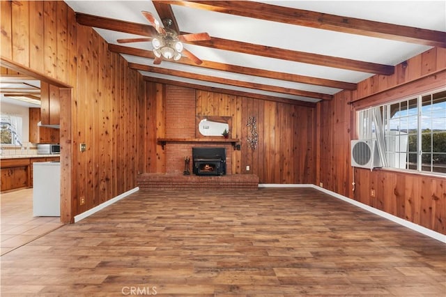 unfurnished living room featuring hardwood / wood-style floors, beamed ceiling, wooden walls, a wood stove, and ceiling fan