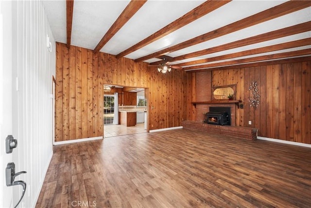 unfurnished living room with ceiling fan, beamed ceiling, a wood stove, and hardwood / wood-style floors