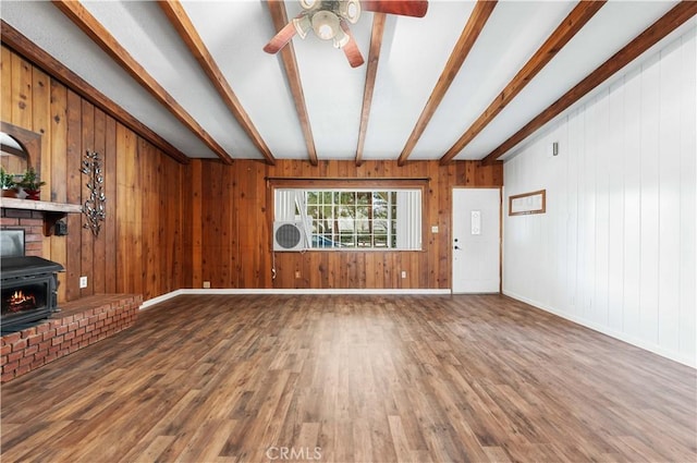 unfurnished living room with ceiling fan, a wood stove, hardwood / wood-style flooring, and beamed ceiling