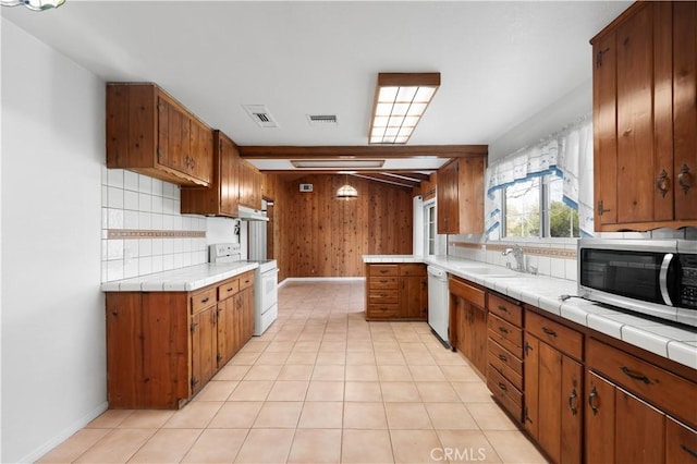 kitchen with tile countertops, sink, wooden walls, white appliances, and beamed ceiling