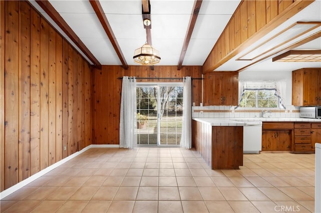 kitchen with decorative light fixtures, tile countertops, wood walls, and white dishwasher