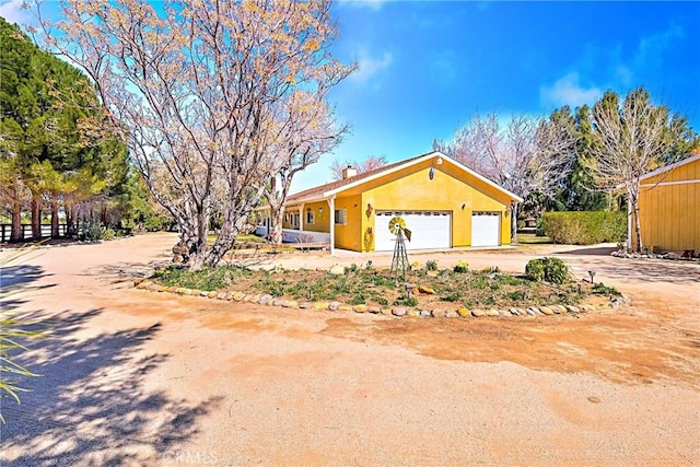 40836 36th St W, Palmdale, CA 93551 - view of front facade with dirt driveway, a garage, a chimney, and stucco siding