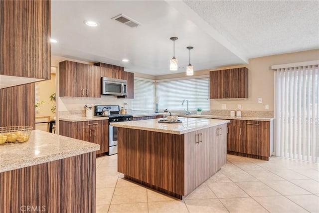 kitchen with appliances with stainless steel finishes, light tile patterned flooring, a textured ceiling, a kitchen island, and pendant lighting