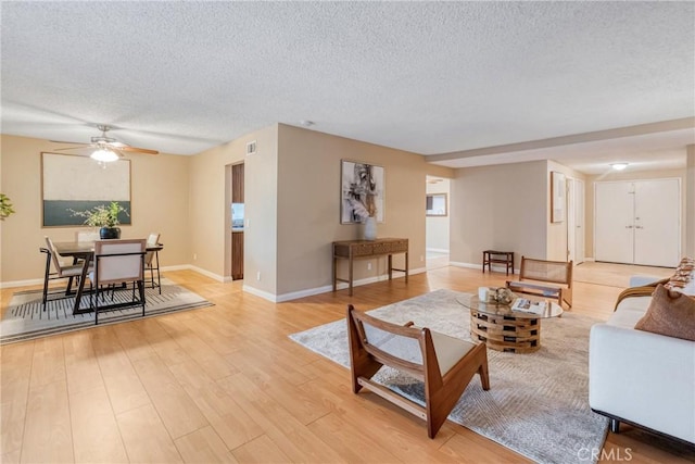 living room featuring ceiling fan, a textured ceiling, and light hardwood / wood-style flooring