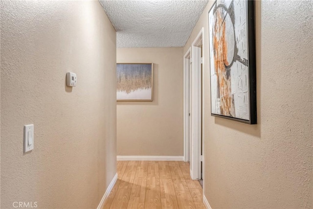 hallway with a textured ceiling and light hardwood / wood-style flooring