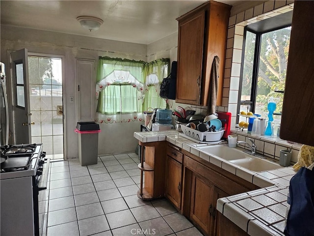 kitchen featuring gas range, light tile patterned floors, sink, and tile countertops