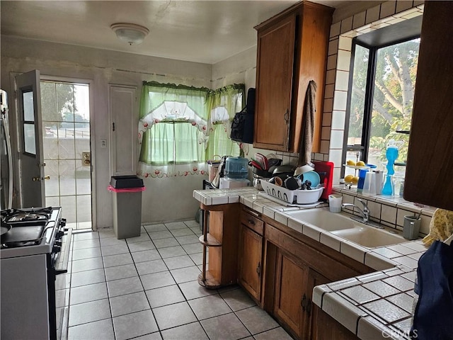 kitchen featuring tile counters, light tile patterned floors, gas range oven, and sink