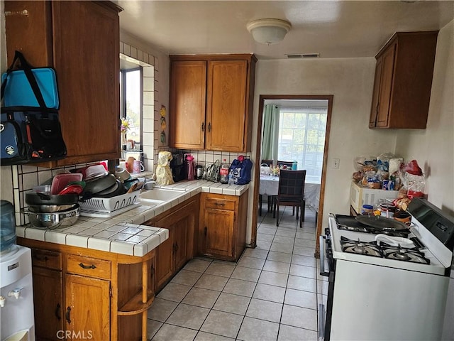 kitchen with light tile patterned flooring, tile countertops, range with gas stovetop, and sink