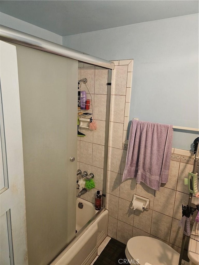 bathroom with toilet, bath / shower combo with glass door, and tile walls