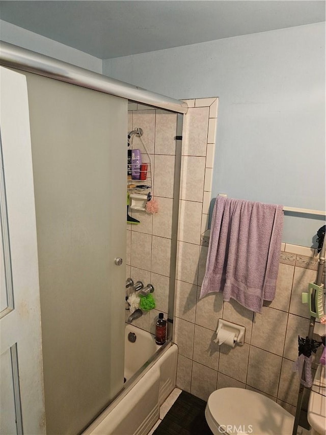 bathroom featuring toilet, tile walls, and shower / bath combination with glass door