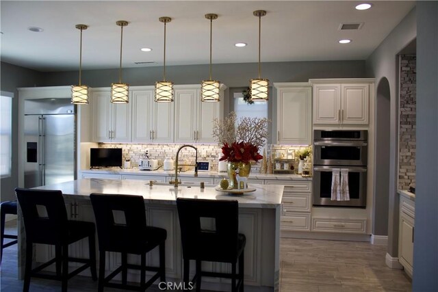 kitchen with backsplash, pendant lighting, appliances with stainless steel finishes, and an island with sink