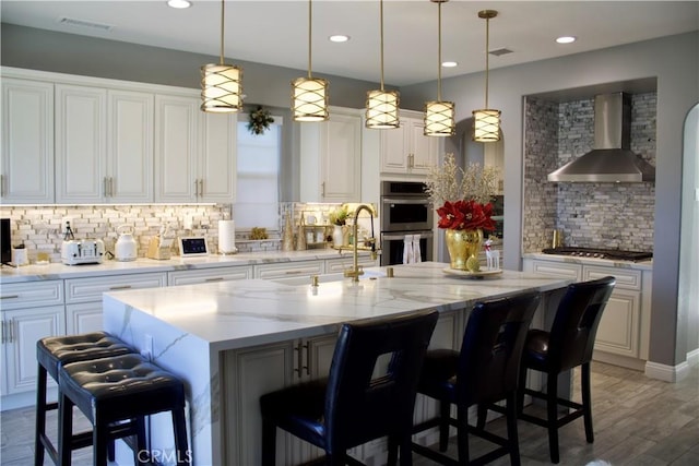 kitchen featuring decorative light fixtures, a spacious island, a breakfast bar, decorative backsplash, and wall chimney exhaust hood