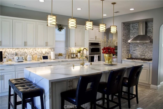 kitchen with pendant lighting, a breakfast bar area, decorative backsplash, a large island, and wall chimney exhaust hood