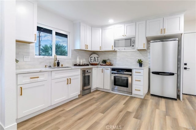 kitchen with tasteful backsplash, white cabinetry, sink, light wood-type flooring, and stainless steel appliances