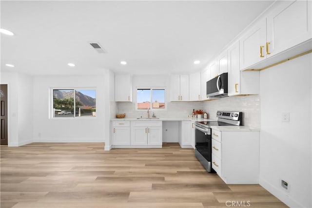 kitchen featuring white cabinets, stainless steel appliances, decorative backsplash, sink, and light wood-type flooring