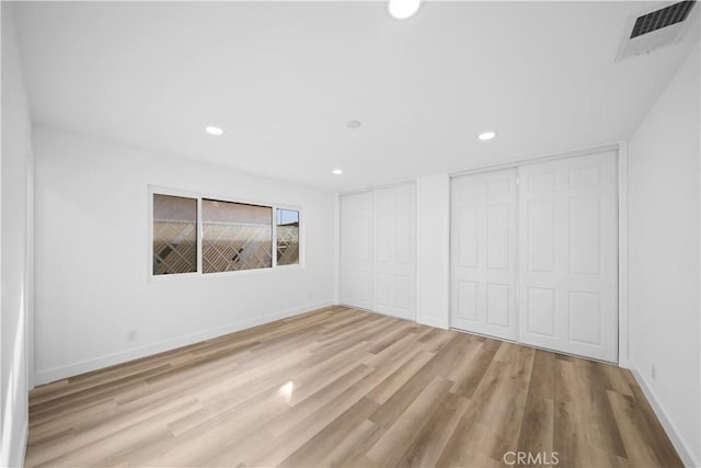 unfurnished bedroom with light hardwood / wood-style flooring and multiple closets