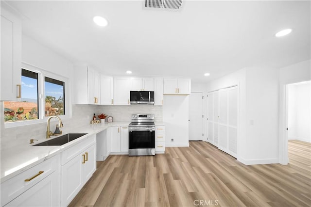 kitchen with white cabinets, sink, light hardwood / wood-style flooring, backsplash, and stainless steel appliances