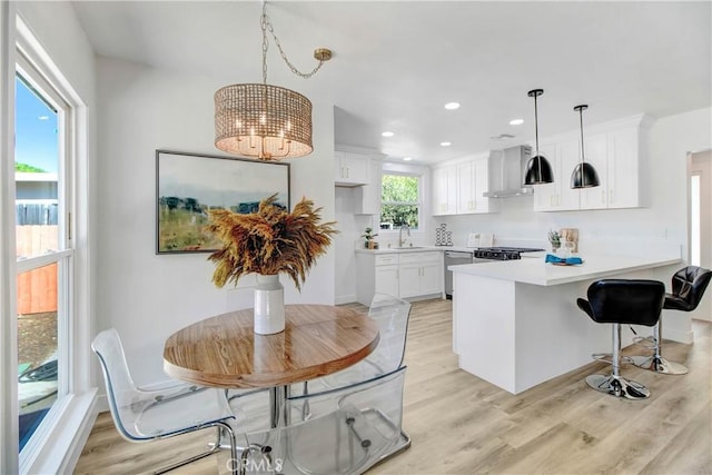 kitchen featuring pendant lighting, dishwasher, white cabinetry, wall chimney range hood, and kitchen peninsula