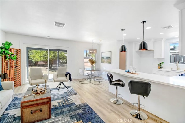 kitchen with pendant lighting, a kitchen bar, white cabinetry, light hardwood / wood-style floors, and sink