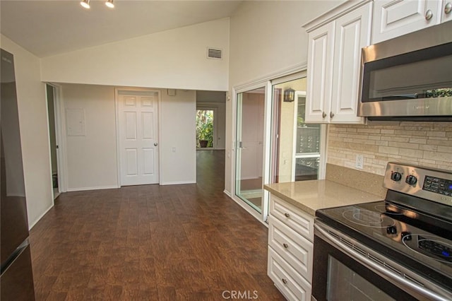 kitchen with appliances with stainless steel finishes, lofted ceiling, white cabinetry, backsplash, and light stone counters