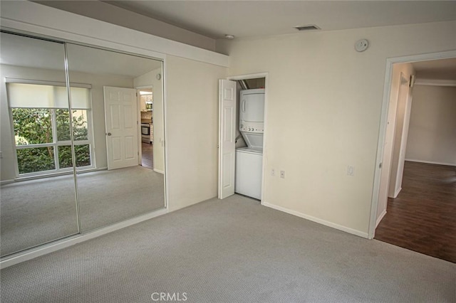 unfurnished bedroom featuring stacked washer and dryer, vaulted ceiling, a closet, and carpet flooring