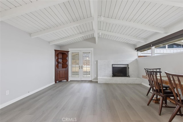 living area featuring wood finished floors, baseboards, vaulted ceiling with beams, a fireplace, and french doors
