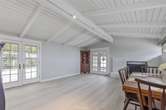 dining area featuring a fireplace, light hardwood / wood-style flooring, vaulted ceiling with beams, and french doors